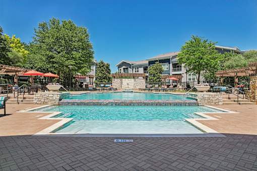 A large outdoor swimming pool surrounded by a stone wall and seating areas.