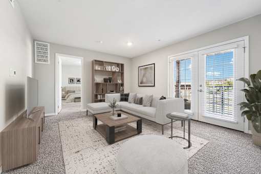 A living room with a white couch, a coffee table, and a large window with blinds.