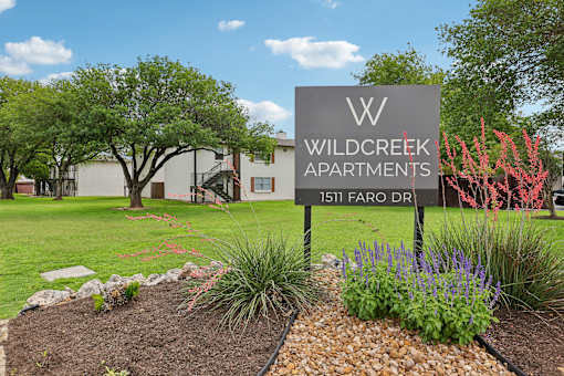 A sign for Wildcreek Apartments stands in front of a building.
