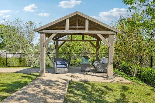 A wooden gazebo with a bench and a table in the middle of a grassy area.