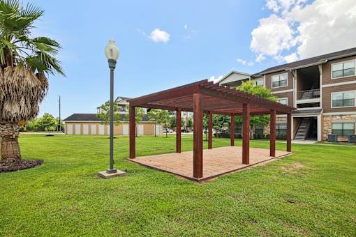 A wooden pavilion is situated in a grassy area in front of a building.