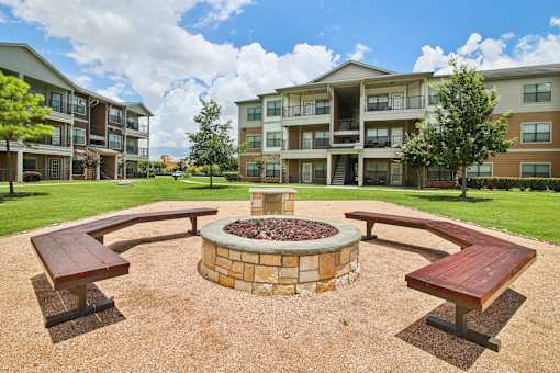 A fire pit sits in the middle of a gravel area with benches on each side.