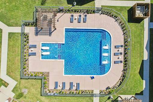 An aerial view of a swimming pool surrounded by a concrete patio and a grassy lawn.