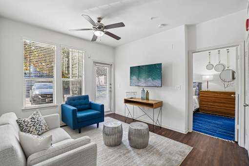 A living room with a white couch, blue chair, and a painting on the wall.