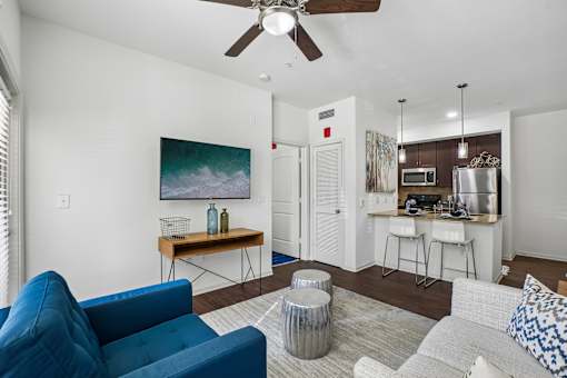 A blue couch sits in a living room with a painting on the wall and a bar area in the background.