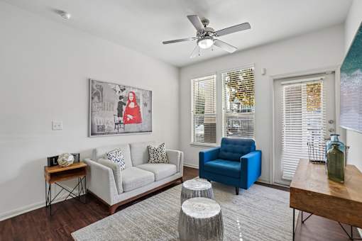A living room with a white couch, a blue chair, and a painting on the wall.