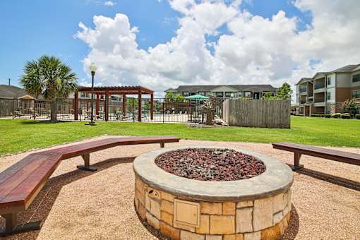 A fire pit in the middle of a playground with benches around it.