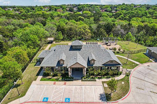 A large building with a grey roof is surrounded by a green lawn and trees.