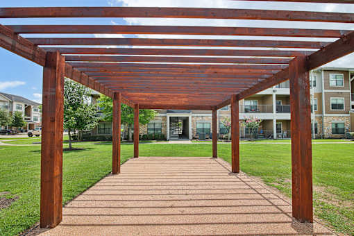 A wooden pergola over a brick walkway in a park.