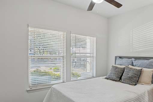 A bedroom with a bed, pillows, and a window with blinds.