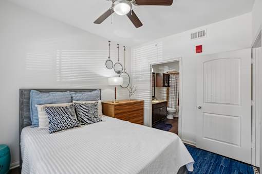 A bedroom with a bed, pillows, a ceiling fan, and a nightstand with a lamp.