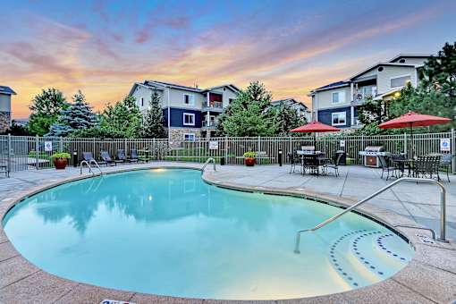A swimming pool surrounded by a fence and chairs with a sunset in the background.