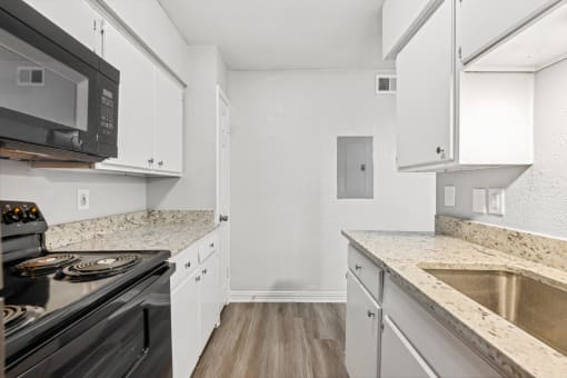 a renovated kitchen with white cabinets and granite counter tops and black appliances