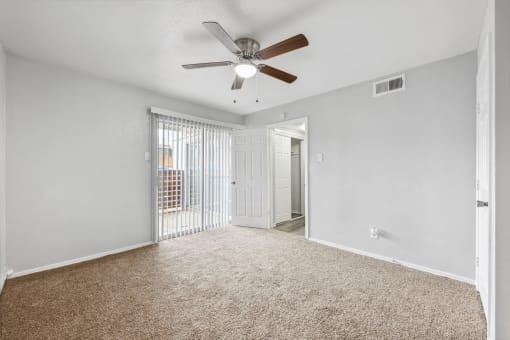 an empty living room with a ceiling fan and a door to a balcony