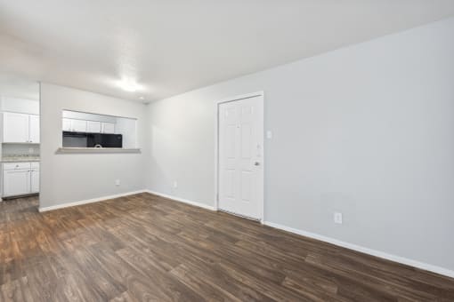 the living room and kitchen of an apartment with wood flooring and white walls