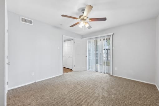 an empty living room with a ceiling fan and a door to a balcony