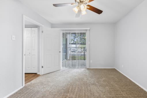 an empty living room with a ceiling fan and a door to a balcony