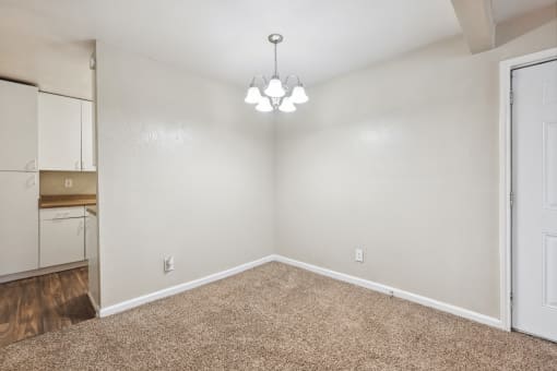 the spacious living room with white walls and carpet and a door to the kitchen