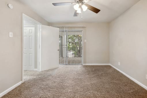 an empty living room with a ceiling fan and a door to a balcony