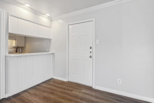 a living room with white walls and a door to a kitchen