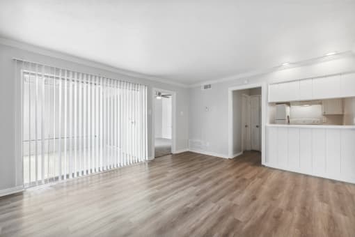 the living room and kitchen of an apartment with white walls and wood floors