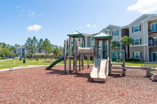 A playground with a green slide and a white slide in front of apartment buildings.