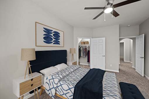 A bedroom with a bed, a ceiling fan, and a painting on the wall.