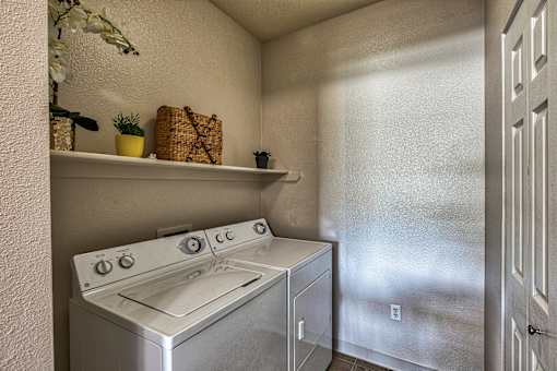 A small kitchen with a stove top oven and a wall-mounted shelf with a plant and a basket on it.