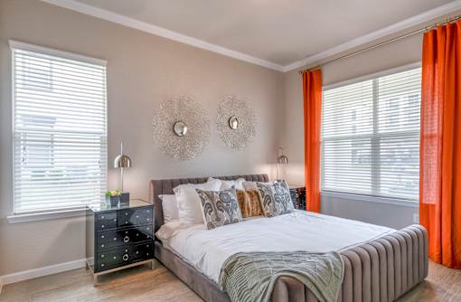 A bedroom with a bed, nightstand, and window with orange curtains.