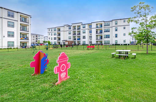 A grassy area in front of apartment buildings with a red fire hydrant and a colorful sculpture.