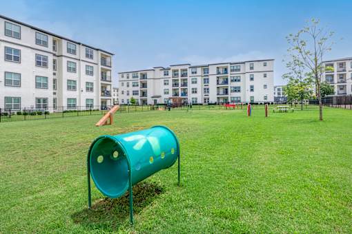 A green tube slide in a grassy area with apartment buildings in the background.