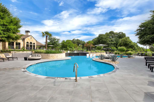 a pool with a stone wall and patio furniture with a house in the background
