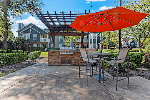 a patio with an umbrella and tables with chairs and a grill