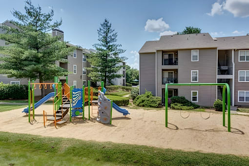 A playground with a slide, swings, and sandbox in front of apartment buildings.
