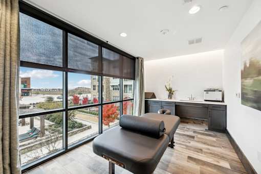 A room with a black chair and a window overlooking a parking lot.