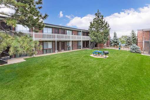 A grassy area in front of a building with a bench and a tree.