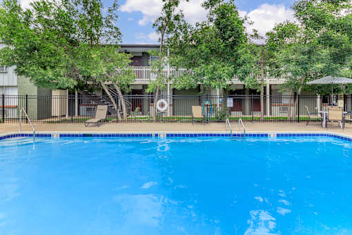 A swimming pool surrounded by trees and a building in the background.