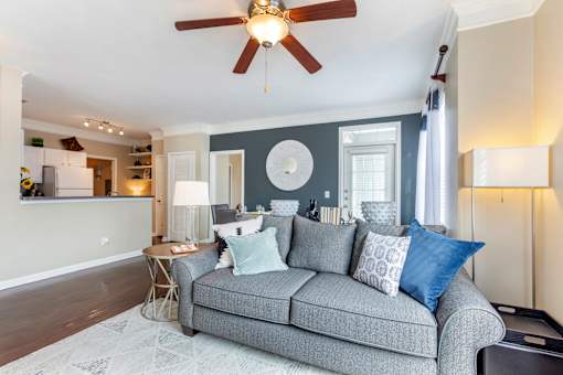 A grey couch with blue pillows is in the center of a room with a ceiling fan.
