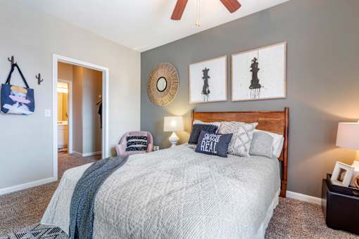 A bedroom with a bed, a ceiling fan, and a wall hanging.