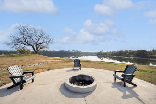 two adirondack chairs sit around a fire pit with a lake in the background