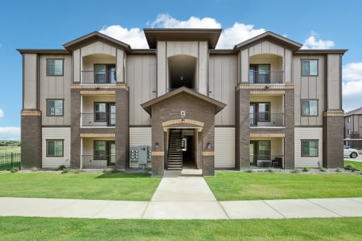 a tan and brown apartment building with a sidewalk and grass