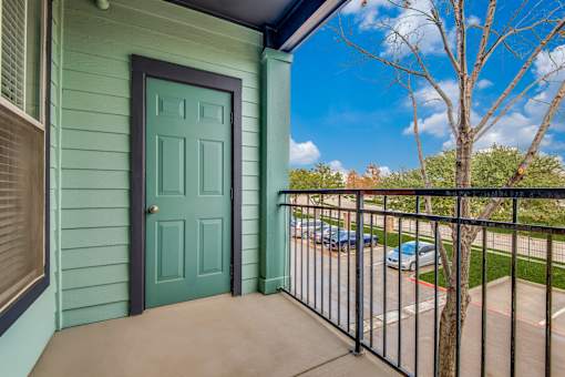 A green door is on a house with a black railing.