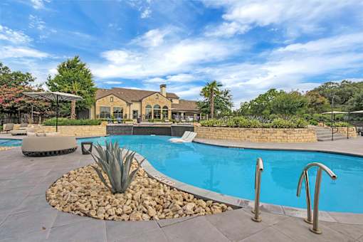 Curved pool edge with stone landscaping, agave plantings, and handrails at entry.
