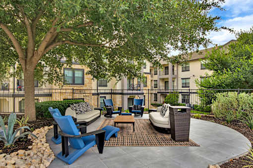Outdoor lounge area with cushioned seating under a shade tree and patterned rug.