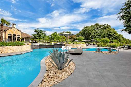 Poolside view with in-water loungers, umbrella seating, and lush green landscaping.