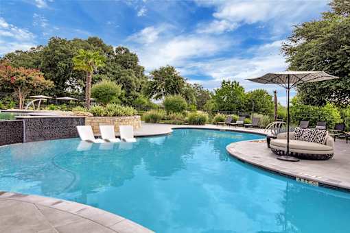 Swimming pool with in-water chaise loungers, shaded daybed, and lounge chairs.