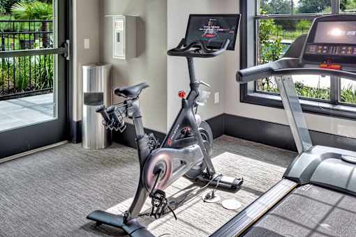 Indoor cardio corner with a stationary bike and treadmill beside bright windows.