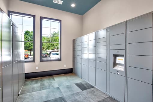 Secure package locker room with electronic kiosks, tall windows, and tiled flooring.