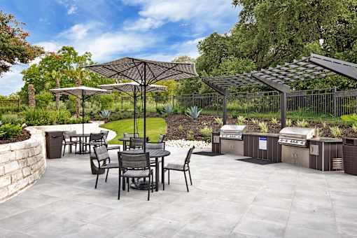 Community grilling pavilion with covered stations, patio tables, and umbrella seating.