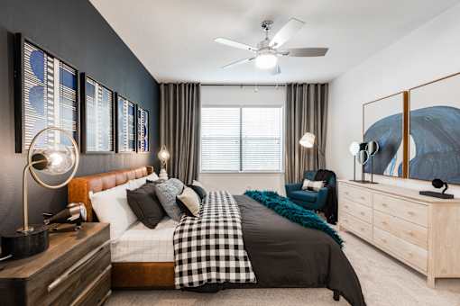 Primary bedroom with ceiling fan, upholstered bed, accent wall, and large window.